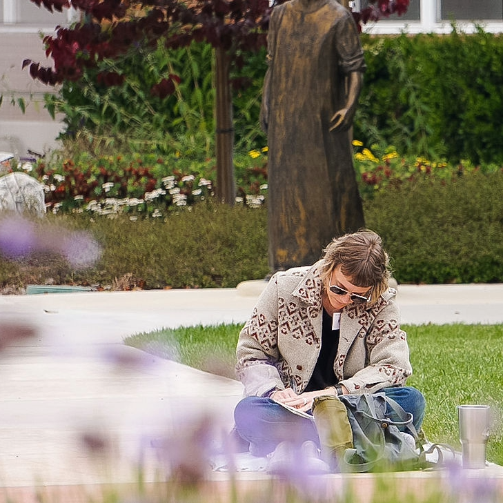A woman sits crosslegged journaling in a garden